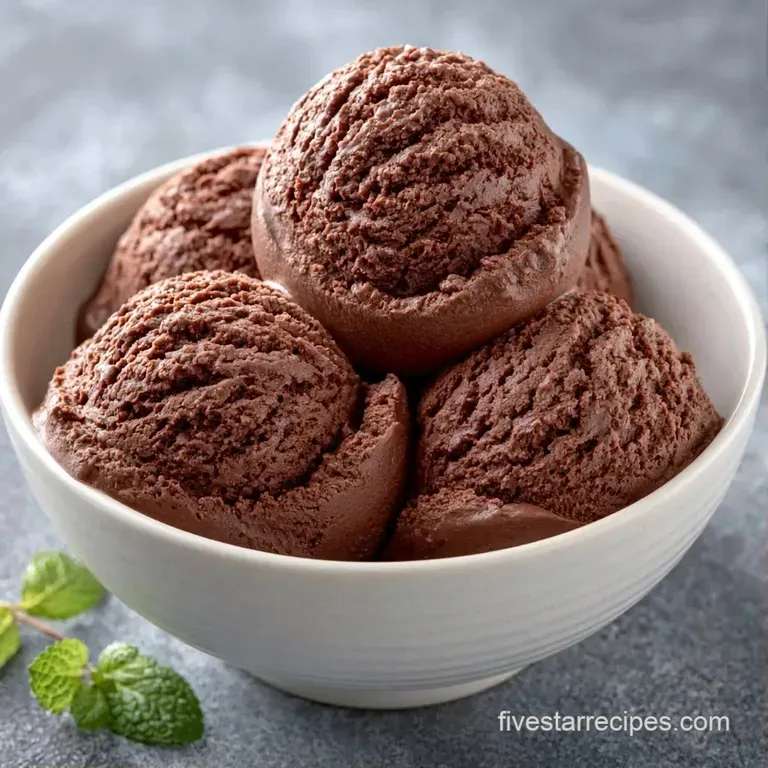 A smooth scoop of frozen cocoa dessert on a dark slate plate, garnished with fresh mint and a ripe raspberry.